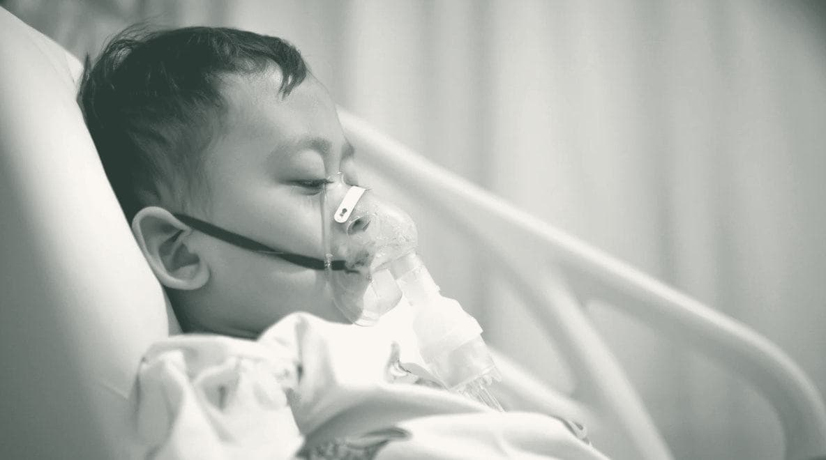 A young child resting in a hospital bed while receiving a breathing treatment
