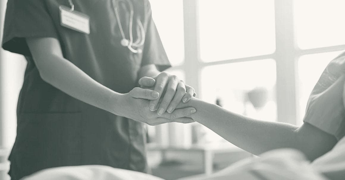 A nurse gently holding a patient's hand at the bedside