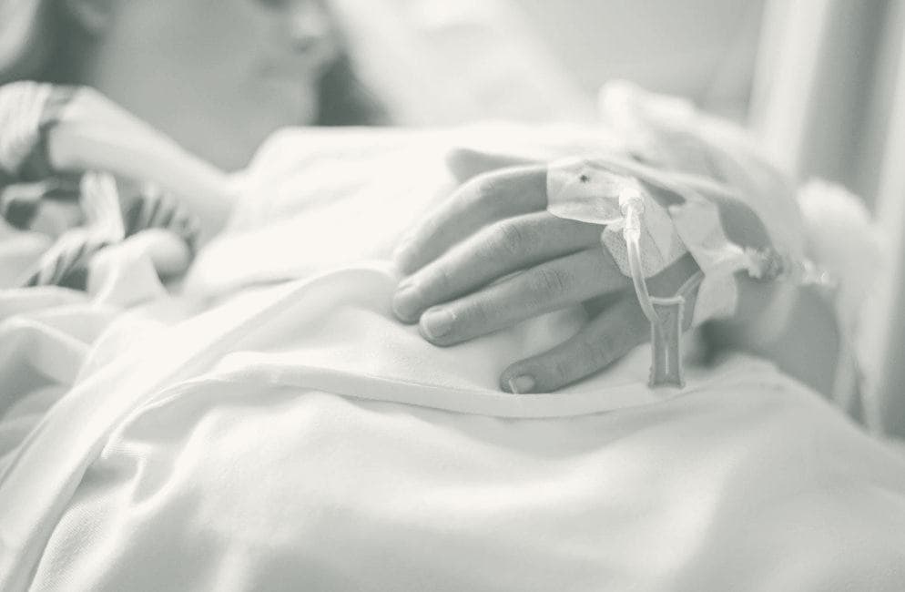 A resting patient's hand with an IV line, tucked under a warm blanket